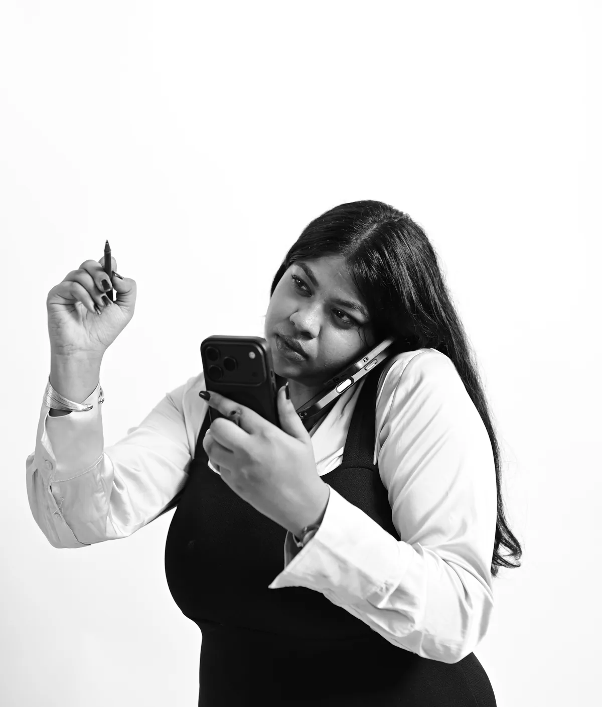 Aratrika Tarafdar on a phone call, holding a second phone and a pen, photographed in black and white
