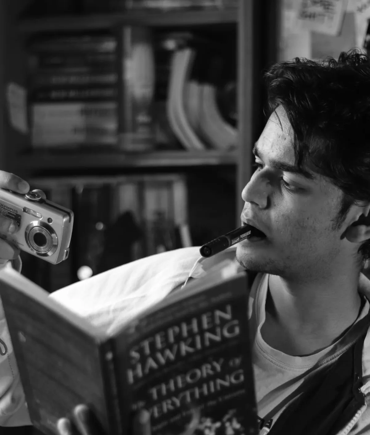 Priyangshu Banerjee holding a camera and a copy of A Brief History of Time, photographed in black and white