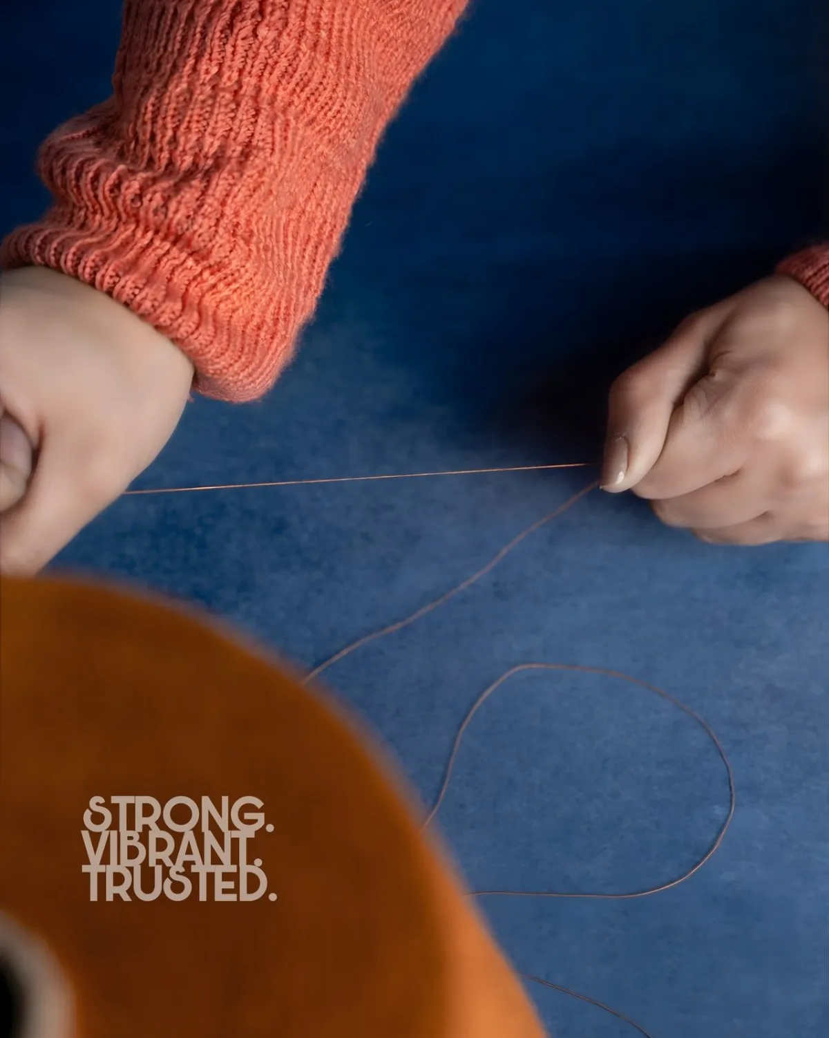 Hands working thread over blue fabric