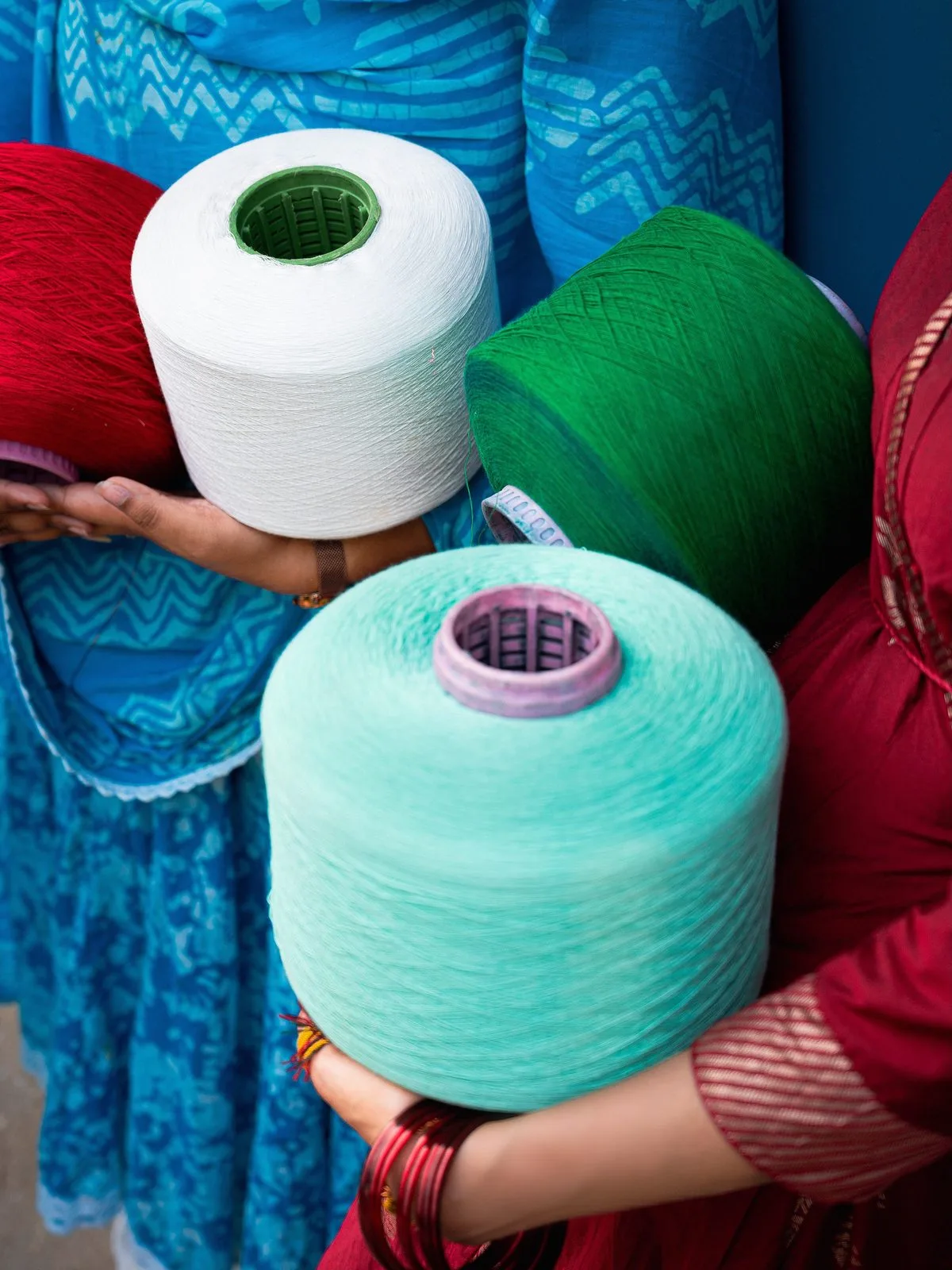 Weavers holding white, green and mint yarn cones